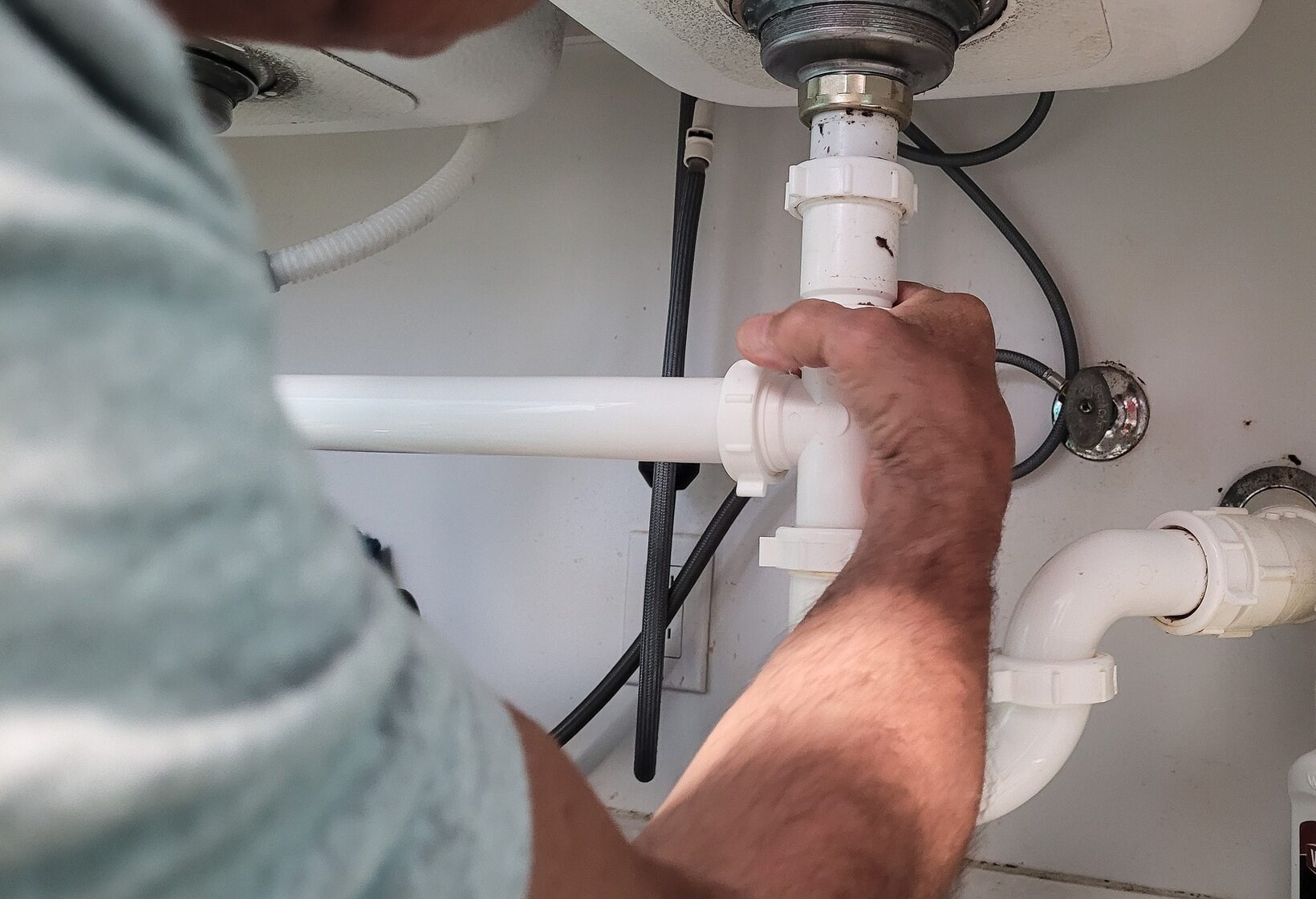 Handyman at home tightening seals on plumbing pipes to stop a leak at kitchen sink.